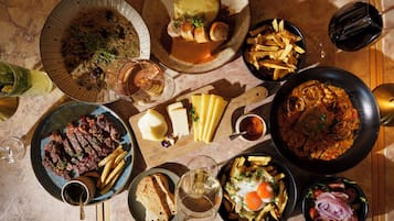A variety of dishes and drinks on a table, including steak, cheese, and a pan of pasta.