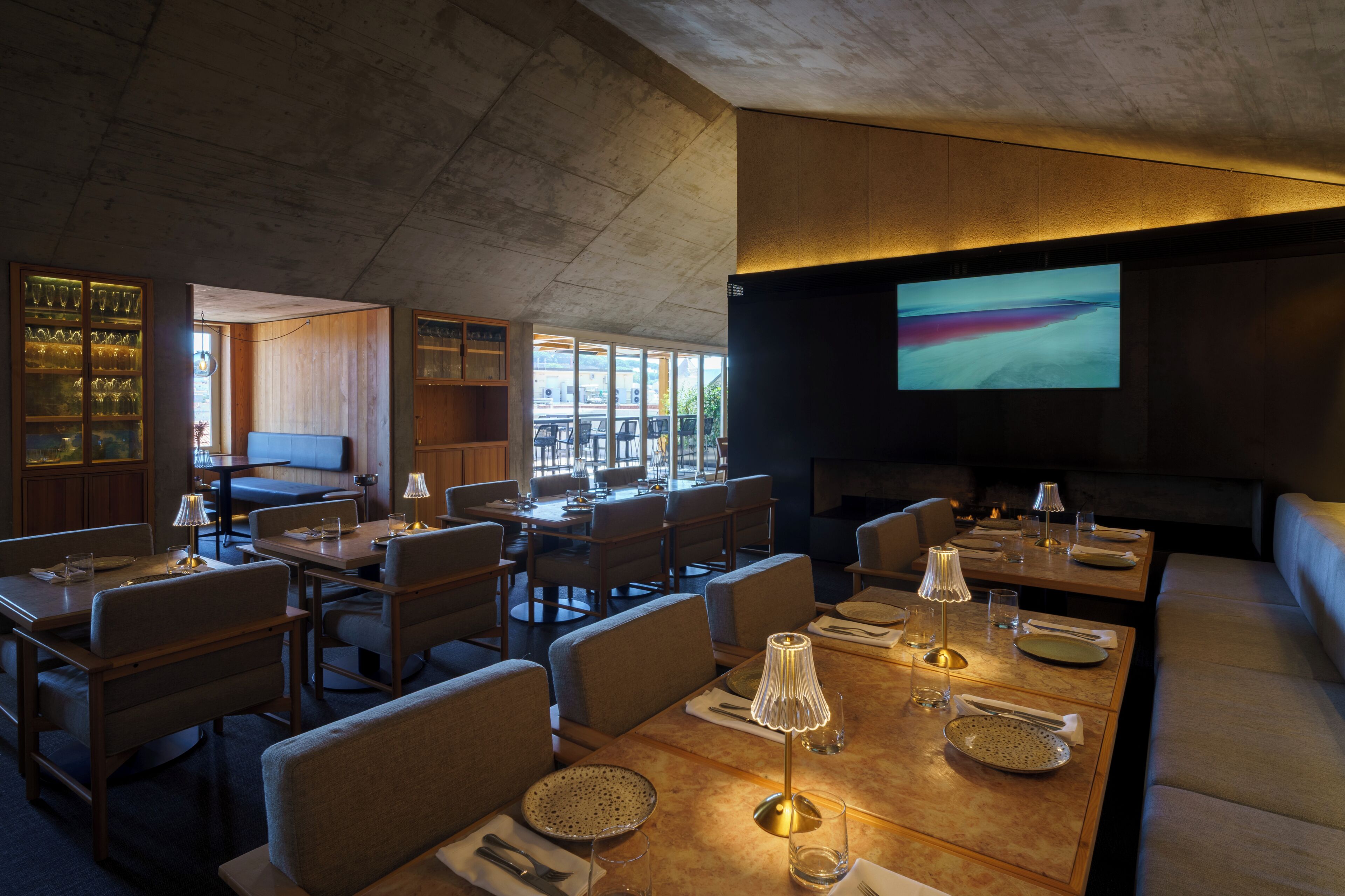 Een restaurant met meerdere eettafels, stoelen en een groot scherm waarop een landschap wordt getoond.