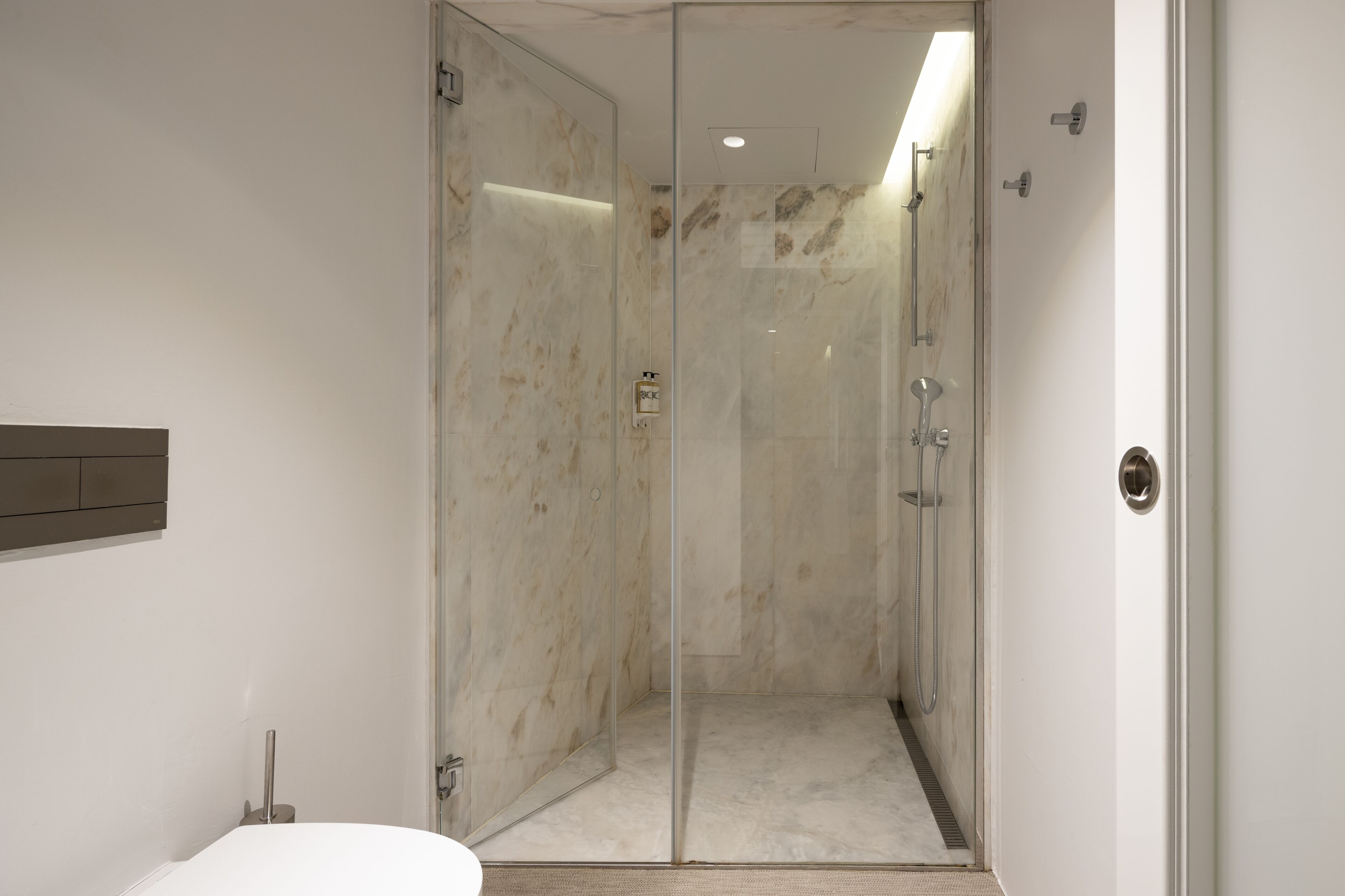 Moderni kylpyhuone, jossa on lasiseinällä erotettu suihku, marmoriseinät ja näkyvissä oleva wc-istuin.
