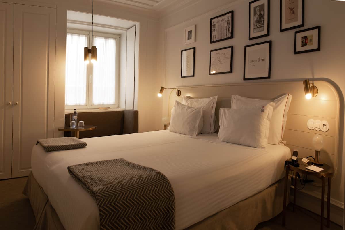 Une chambre d’hôtel avec un grand lit, des tables de chevet, une fenêtre avec des rideaux et des tableaux encadrés accrochés au mur.