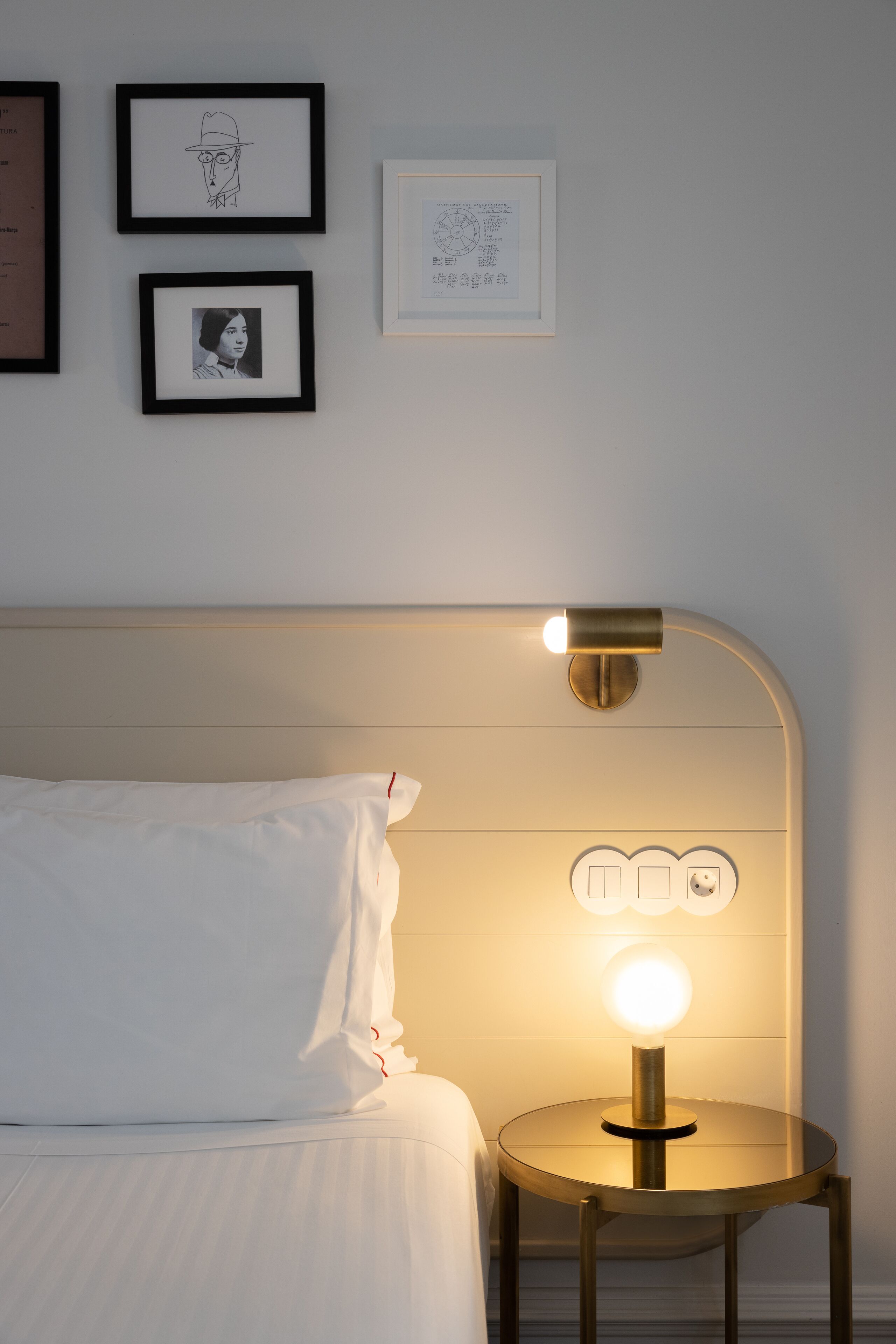 A neatly made bed with white linens, a bedside table with a lamp, and framed artwork on the wall.