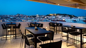 An outdoor dining area with tables and chairs, overlooking a cityscape at dusk. - Lisboa Pessoa Hotel (Lisbon)