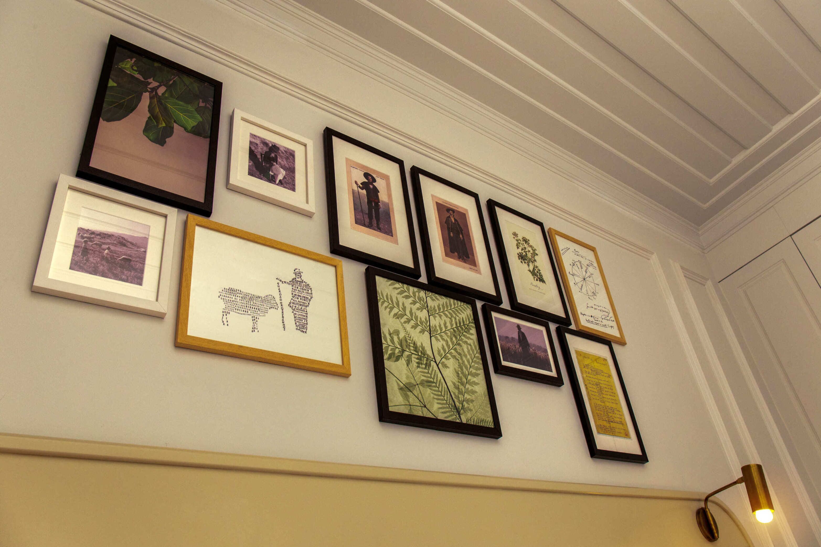 A wall with various framed artworks including botanical prints and portraits.