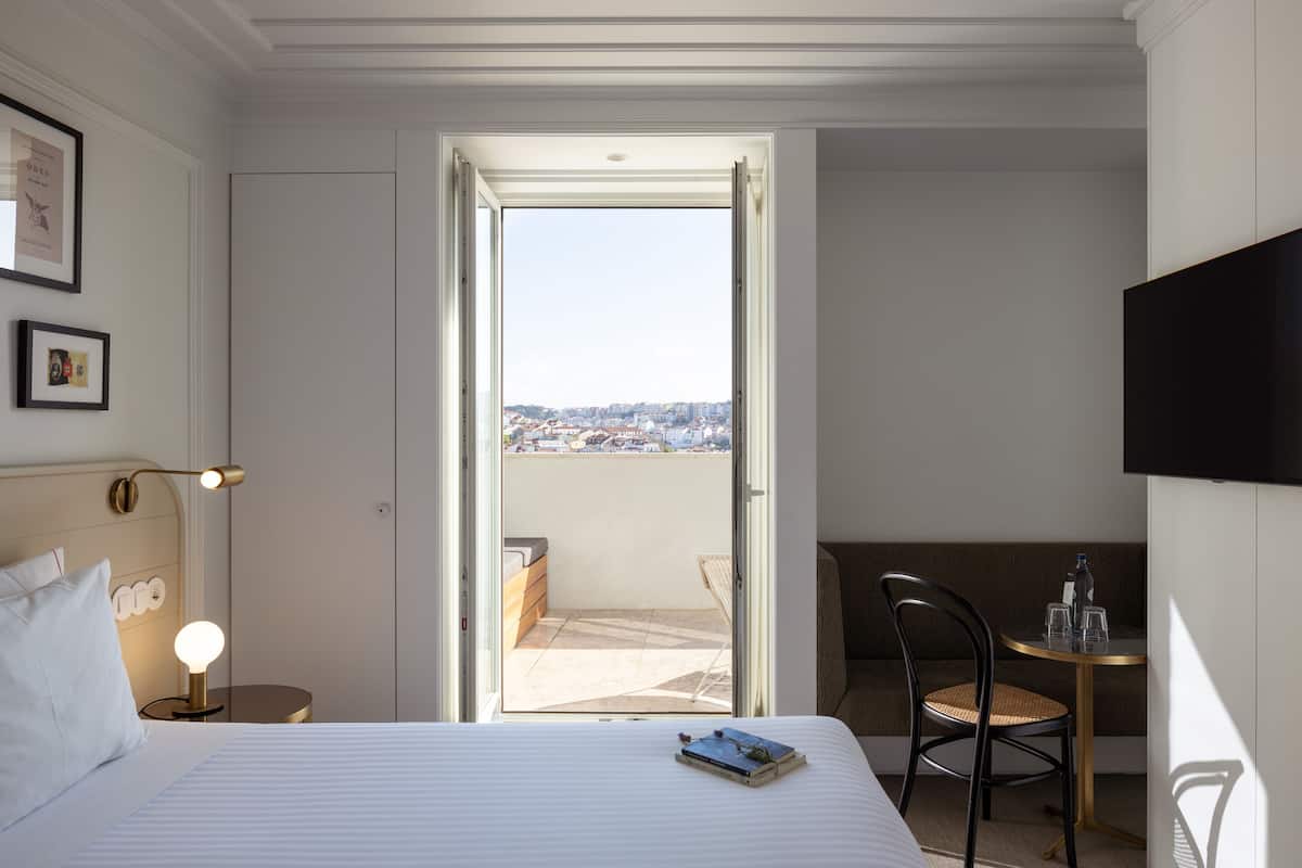 Une chambre d’hôtel avec un lit, une lampe de chevet, une chaise, une petite table avec une bouteille et des verres, et un téléviseur fixé au mur.
