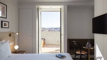 Una camera d'albergo con un letto, una lampada da comodino, una sedia, un tavolino con una bottiglia e dei bicchieri, e una TV montata a parete.