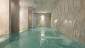 Een wellnessruimte met een marmeren vloer en wanden, een centraal lichtarmatuur en een waterpartij.