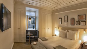 Een hotelkamer met een groot bed, een zithoek met een tafel en stoelen, en een raam met uitzicht op de straat.