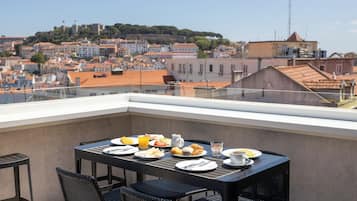 Un balcon avec une table dressée pour le petit-déjeuner, d’où l’on peut admirer un panorama sur la ville, avec ses bâtiments et une colline.