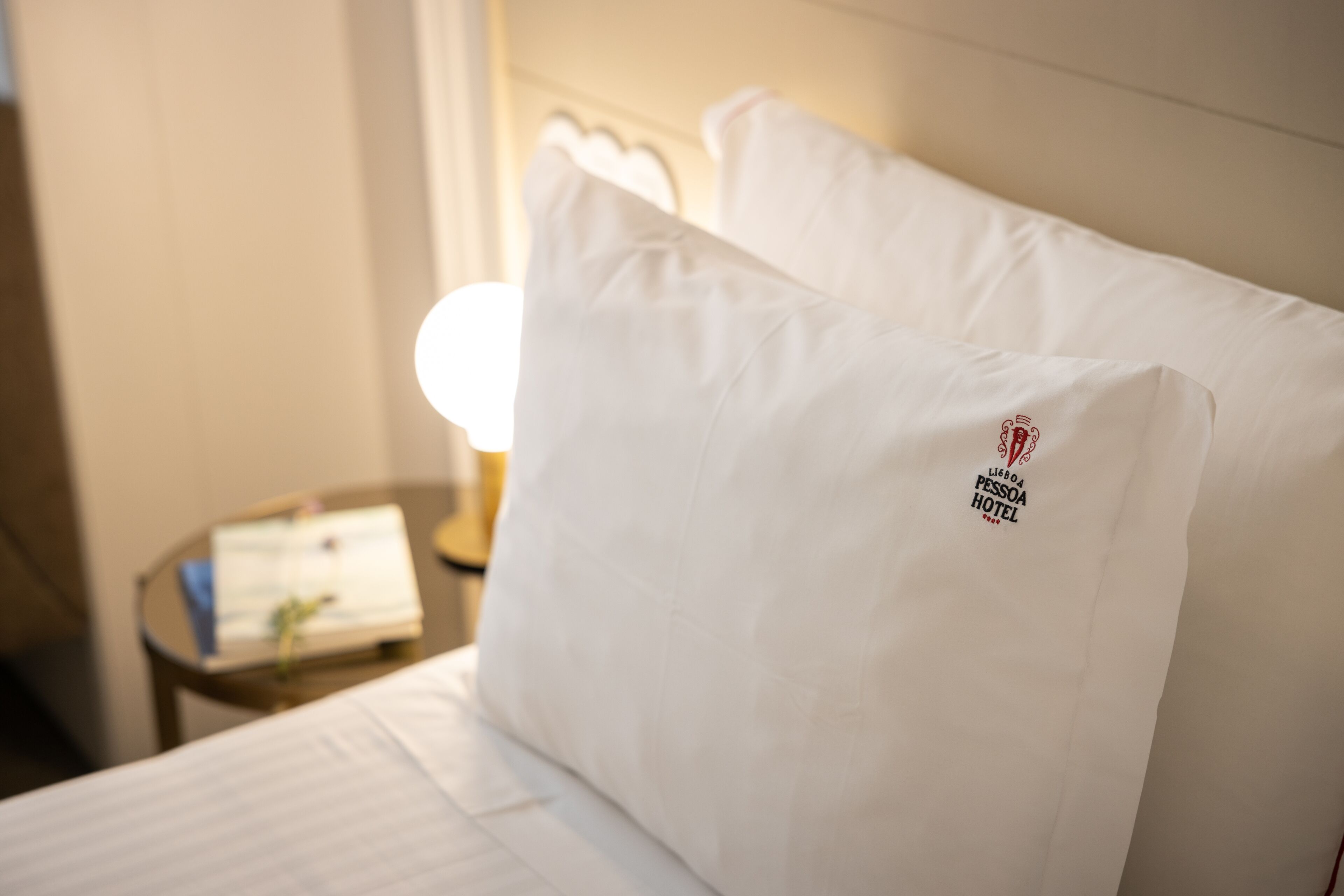 Una habitación de hotel con una cama bien hecha, una mesita de noche con una lámpara y un reloj en la pared.