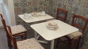 Et spiseområde med et hvidt bord og fire træstole med mønstrede hynder.