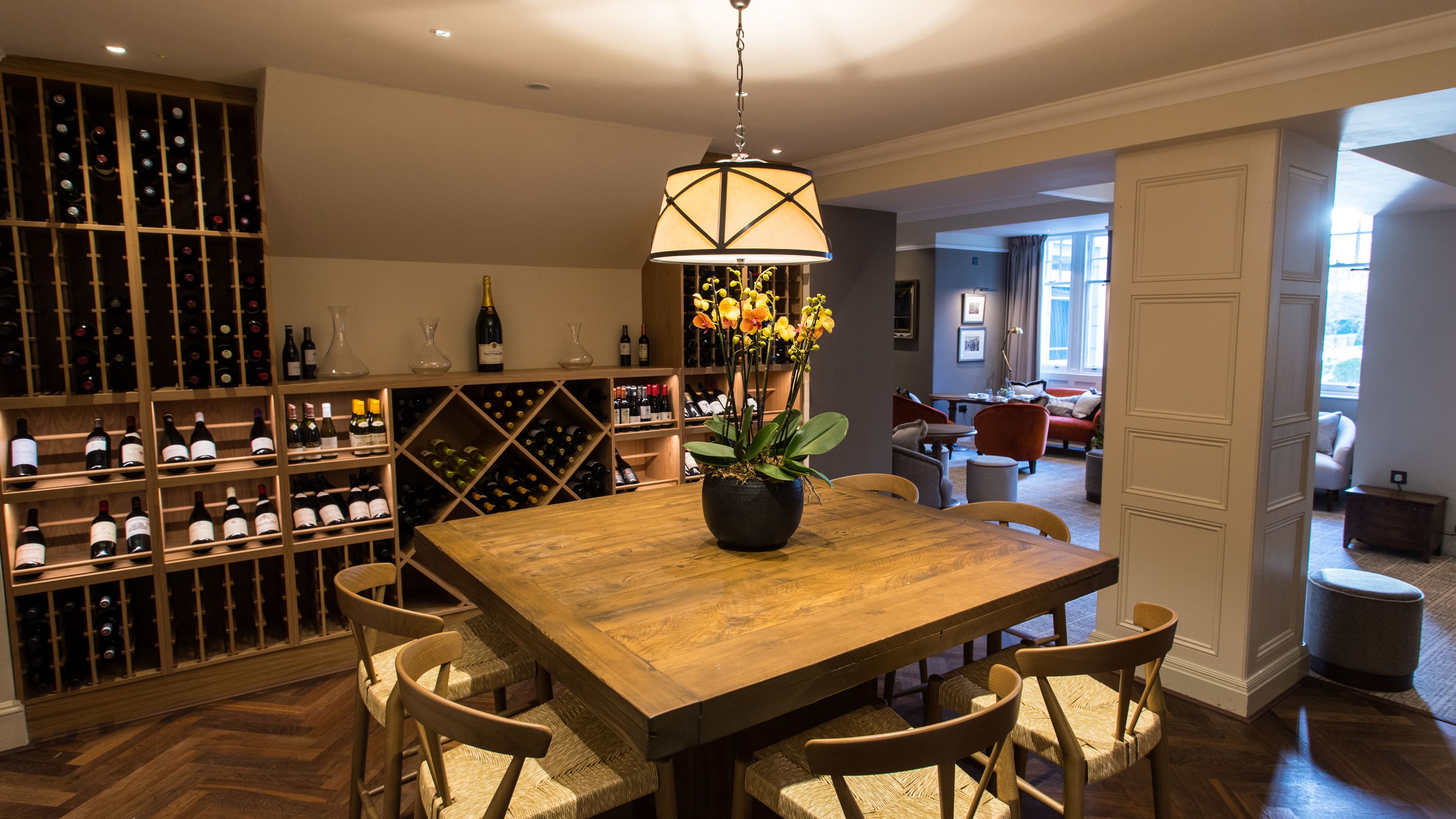 A dining area with a wooden table and chairs, a potted plant, and wine bottles on shelves.