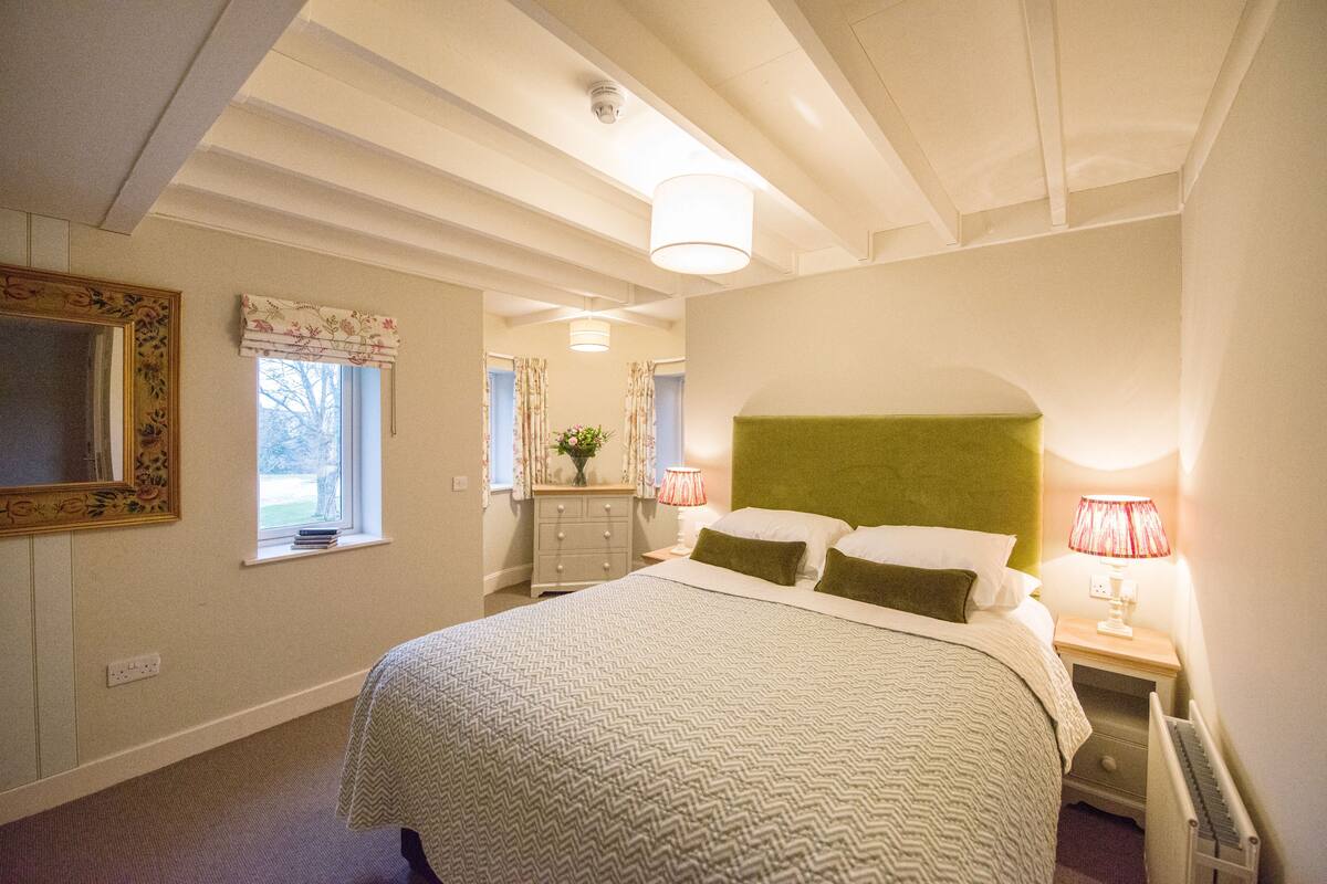 A bedroom with a bed, bedside lamps, a dresser, and a window.