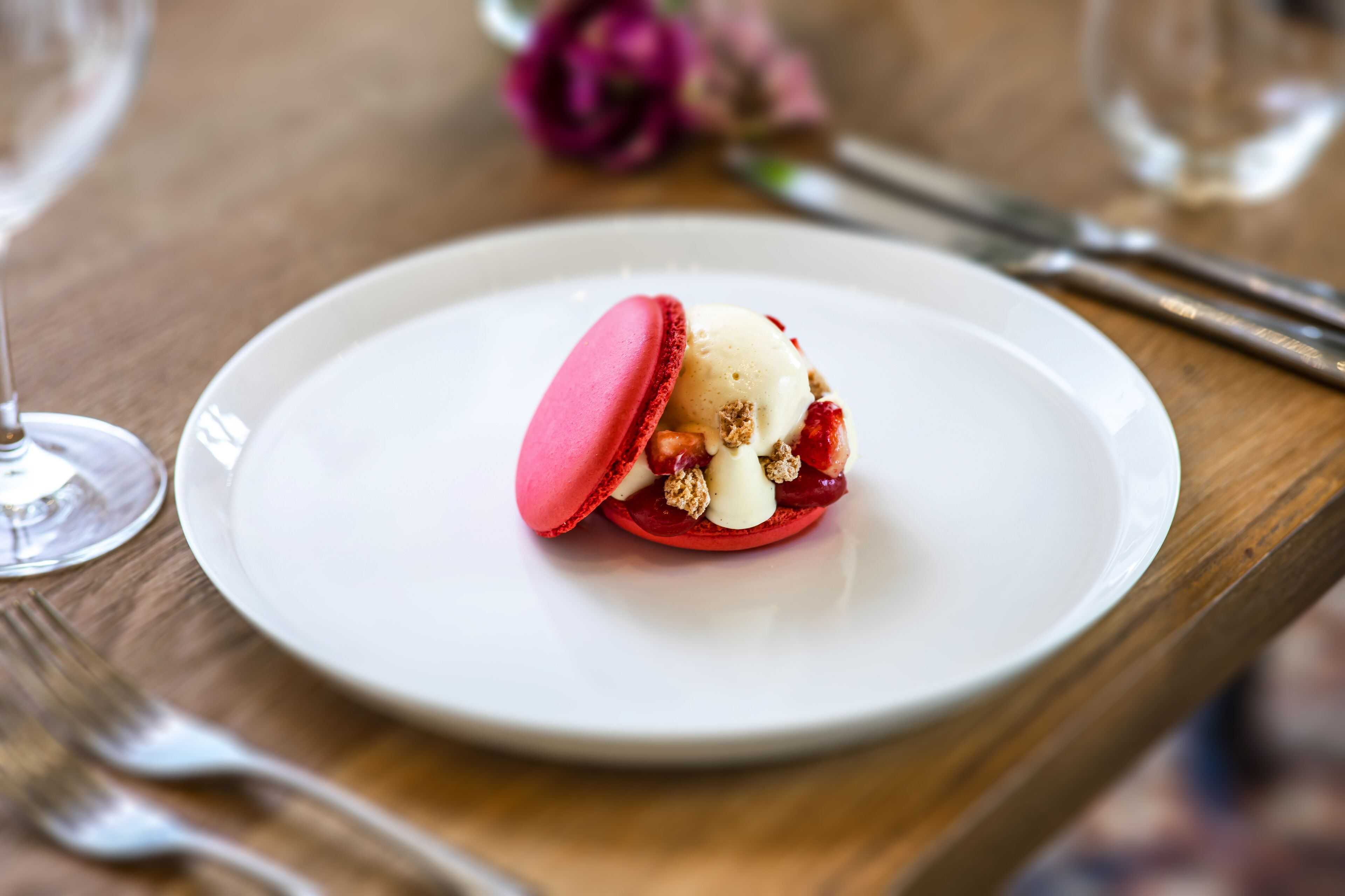 Ein Dessert auf einem weißen Teller, mit einer Gabel und einem Weinglas in der Nähe.