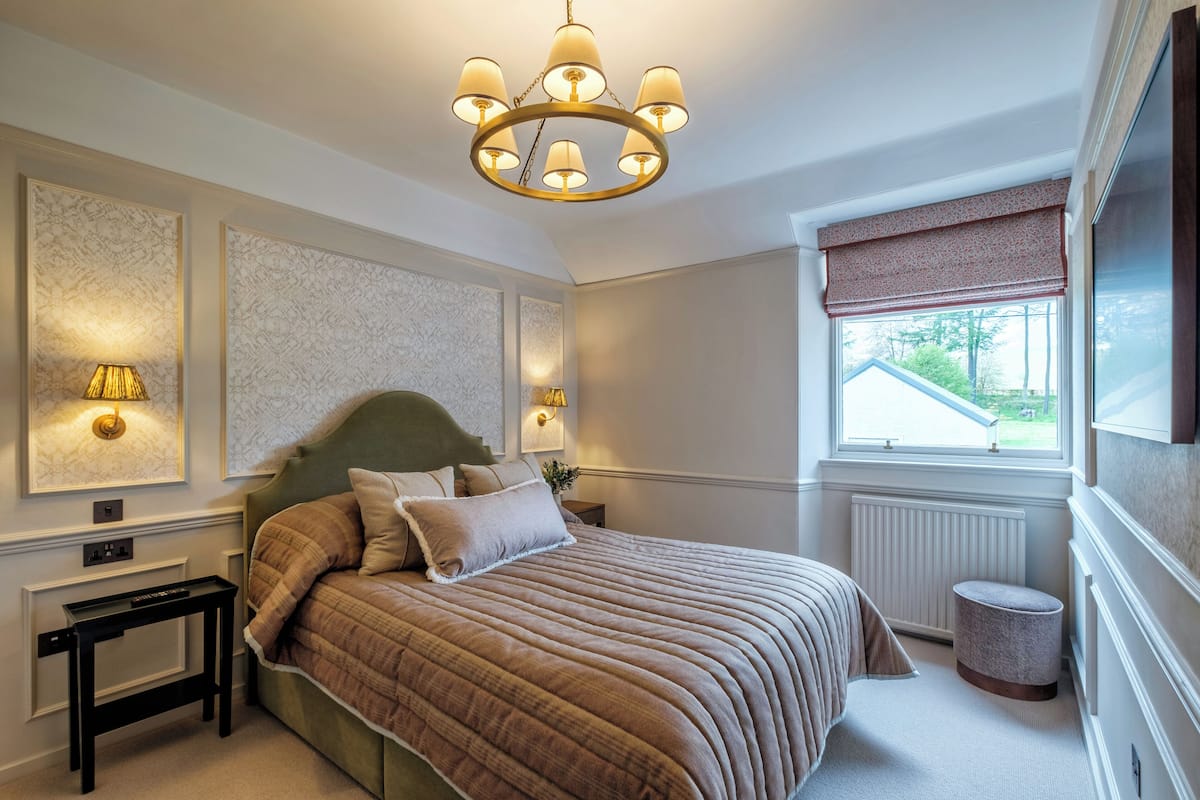 A bedroom with a large bed, a chandelier, a radiator, and a window with a view.