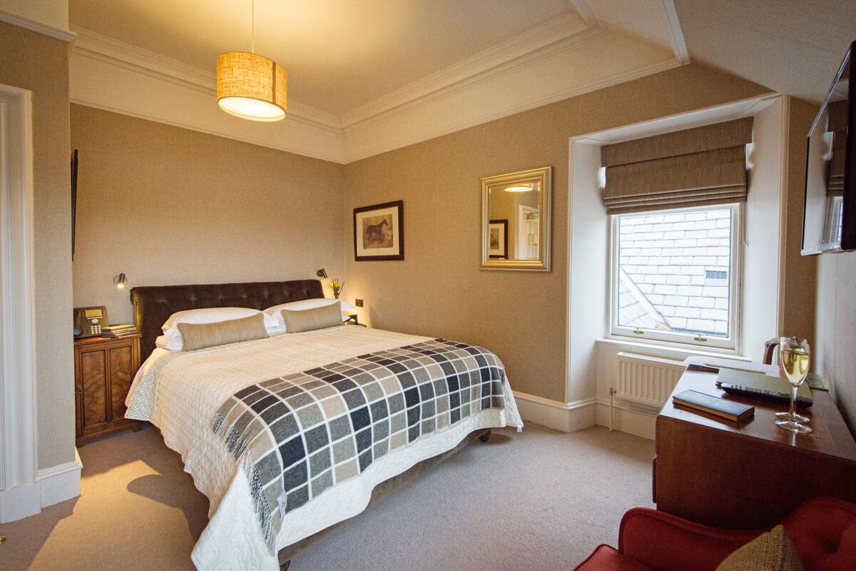 A bedroom with a bed, bedside table, lamp, and a window with a view.