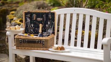 Un montaje para picnic sobre un banco blanco, con una cesta de mimbre que contiene comida, una botella y utensilios.