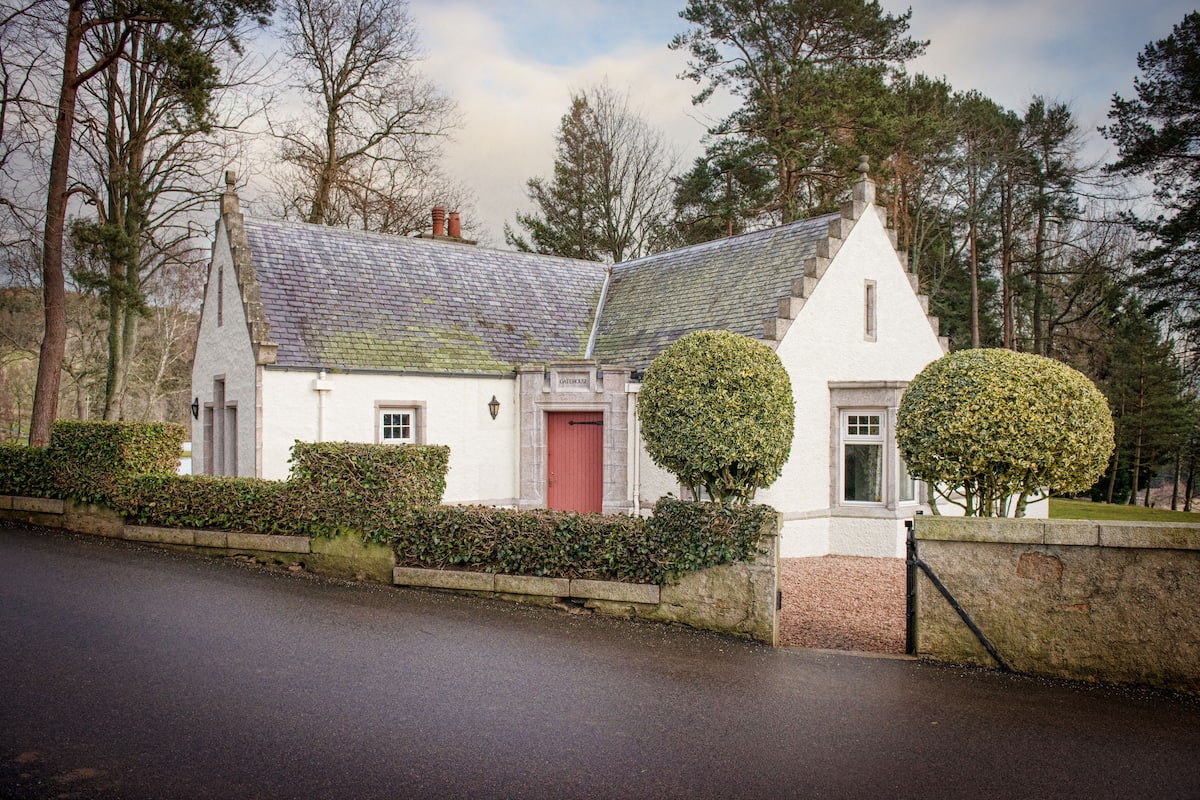 A traditional white house with a red door, a stone wall, and two well-maintained hedges.