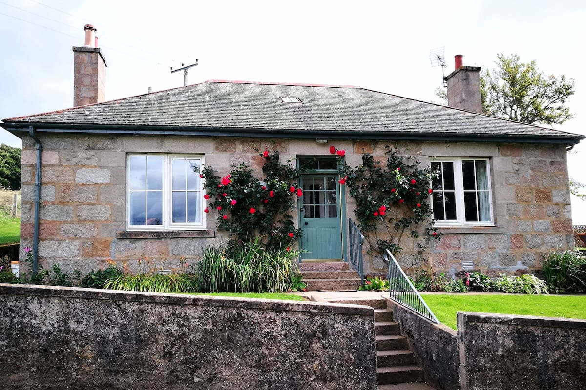 A stone house with a green door, two windows, and a chimney.