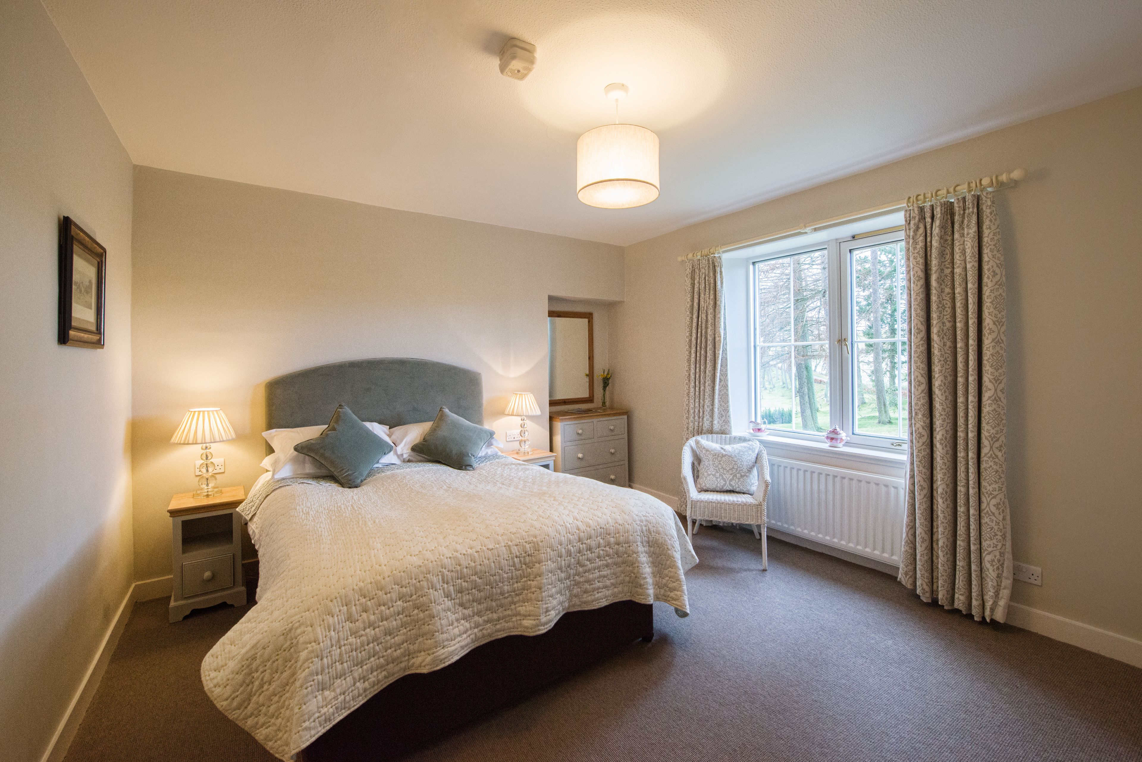 A bedroom with a large bed, bedside lamps, a chair, a window with curtains, and a radiator.