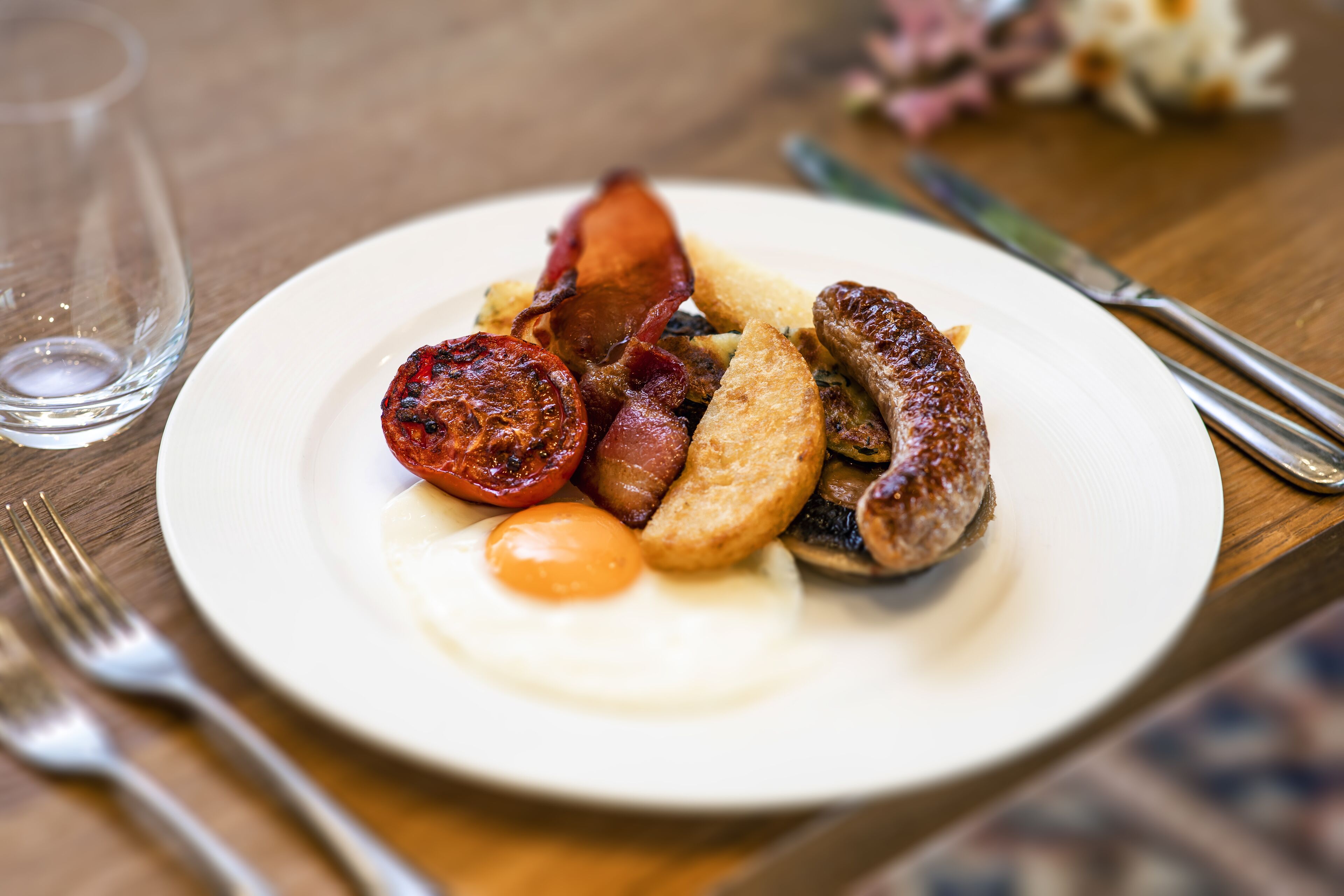Un plato de comida para el desayuno con salchichas, tocino, huevos y tomates.