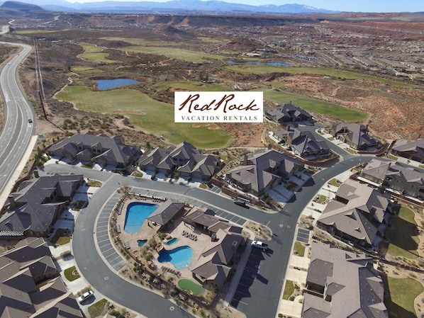 A residential area with modern houses, a swimming pool, and a golf course in the background.