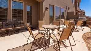 Un patio amueblado con mobiliario exterior, como una mesa, sillas y una parrilla.