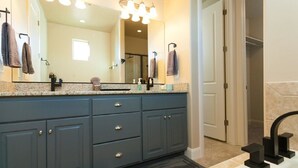 Un baño con un espejo grande, armarios azul oscuro, encimera blanca y grifo negro.
