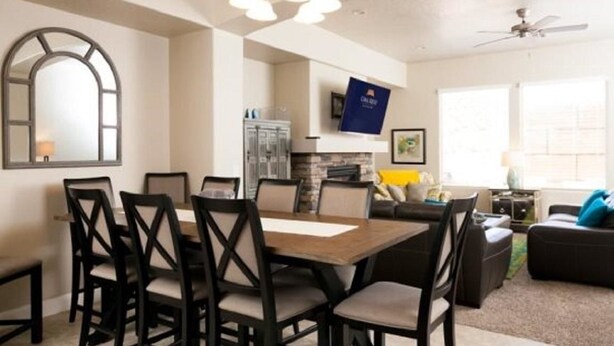 Un comedor con una mesa rectangular y seis sillas, una zona de cocina con armarios y un microondas, y un salón con un sofá y una televisión.