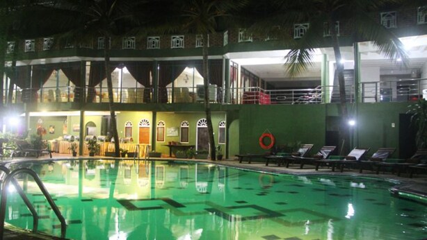 A swimming pool with lounge chairs, a lifebuoy, and a building with multiple windows and balconies. - Hotel Eden Garden (Inamaluwa)