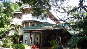 A traditional building with a covered patio area, surrounded by lush greenery and a paved walkway. - Hotel Eden Garden (Inamaluwa)
