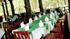 A restaurant with long tables covered in green tablecloths, white napkins, and red chairs. - Hotel Eden Garden (Inamaluwa)