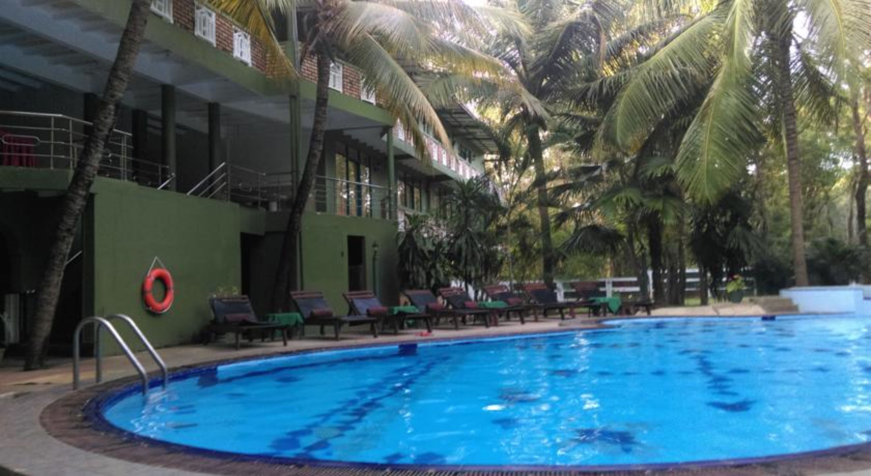 A swimming pool surrounded by lounge chairs and palm trees, with a building in the background.