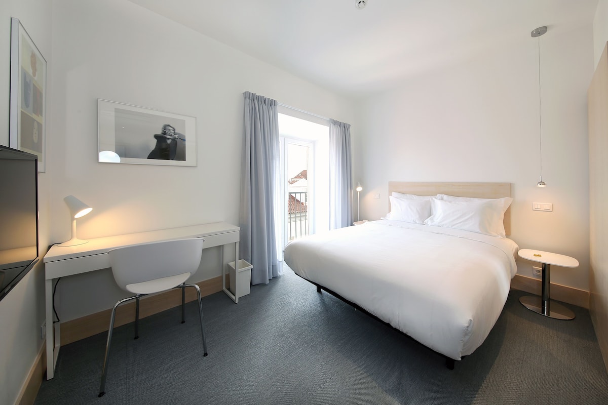 Una habitación de hotel con cama, escritorio, silla y una mesita.