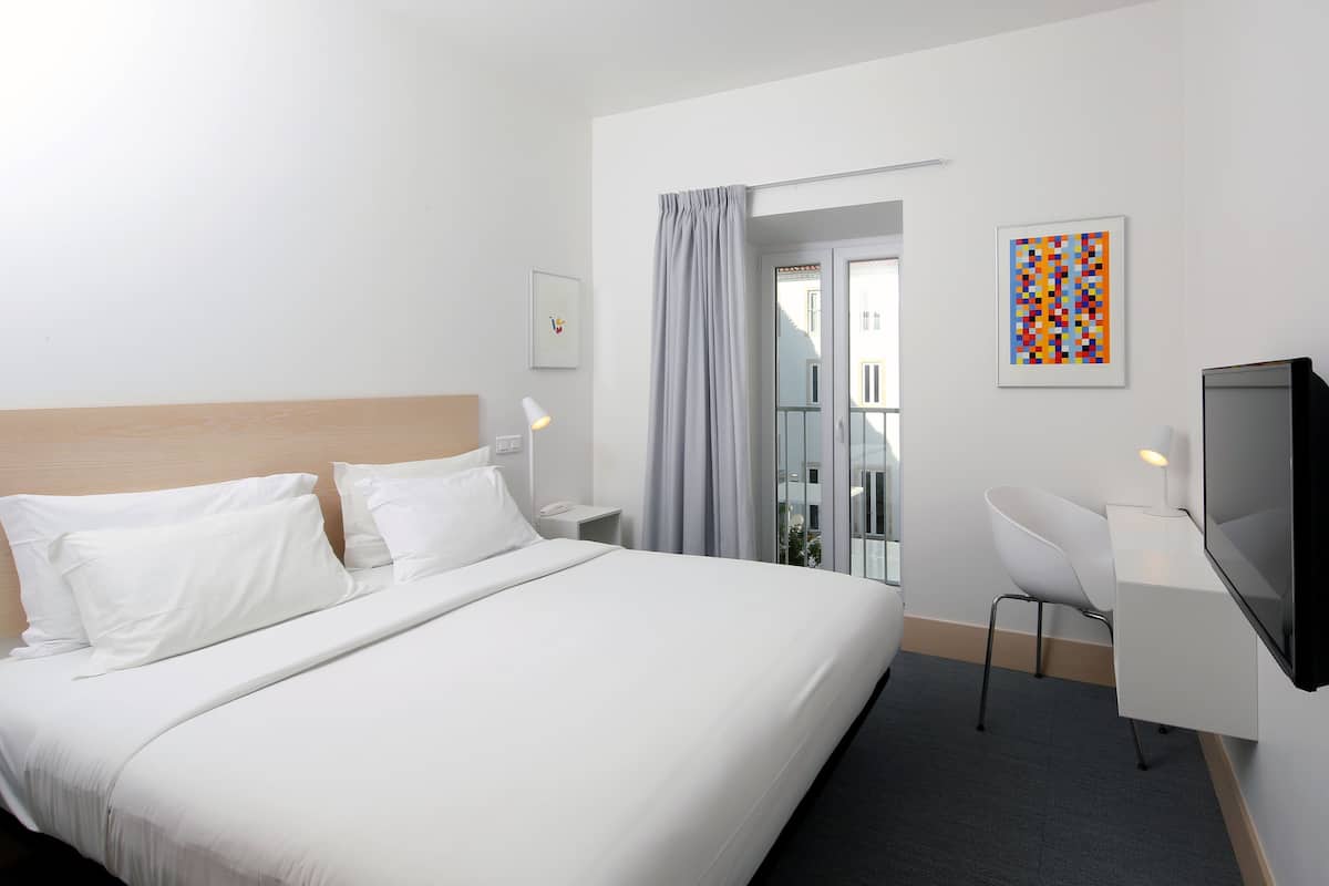 Una habitación de hotel con una cama grande, un escritorio con una silla, un televisor y una ventana con cortinas.