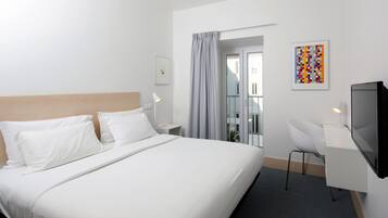Een hotelkamer met een groot bed, een bureau met stoel, een televisie en een raam met gordijnen.