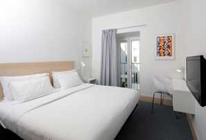Une chambre d’hôtel avec un grand lit, un bureau avec une chaise, une télévision et une fenêtre avec des rideaux.