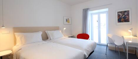 A hotel room with two beds, a desk, a chair, and a window with curtains.