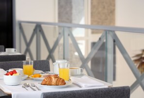 Une table de petit-déjeuner avec des croissants, des fruits, du jus d’orange et des tasses de café.