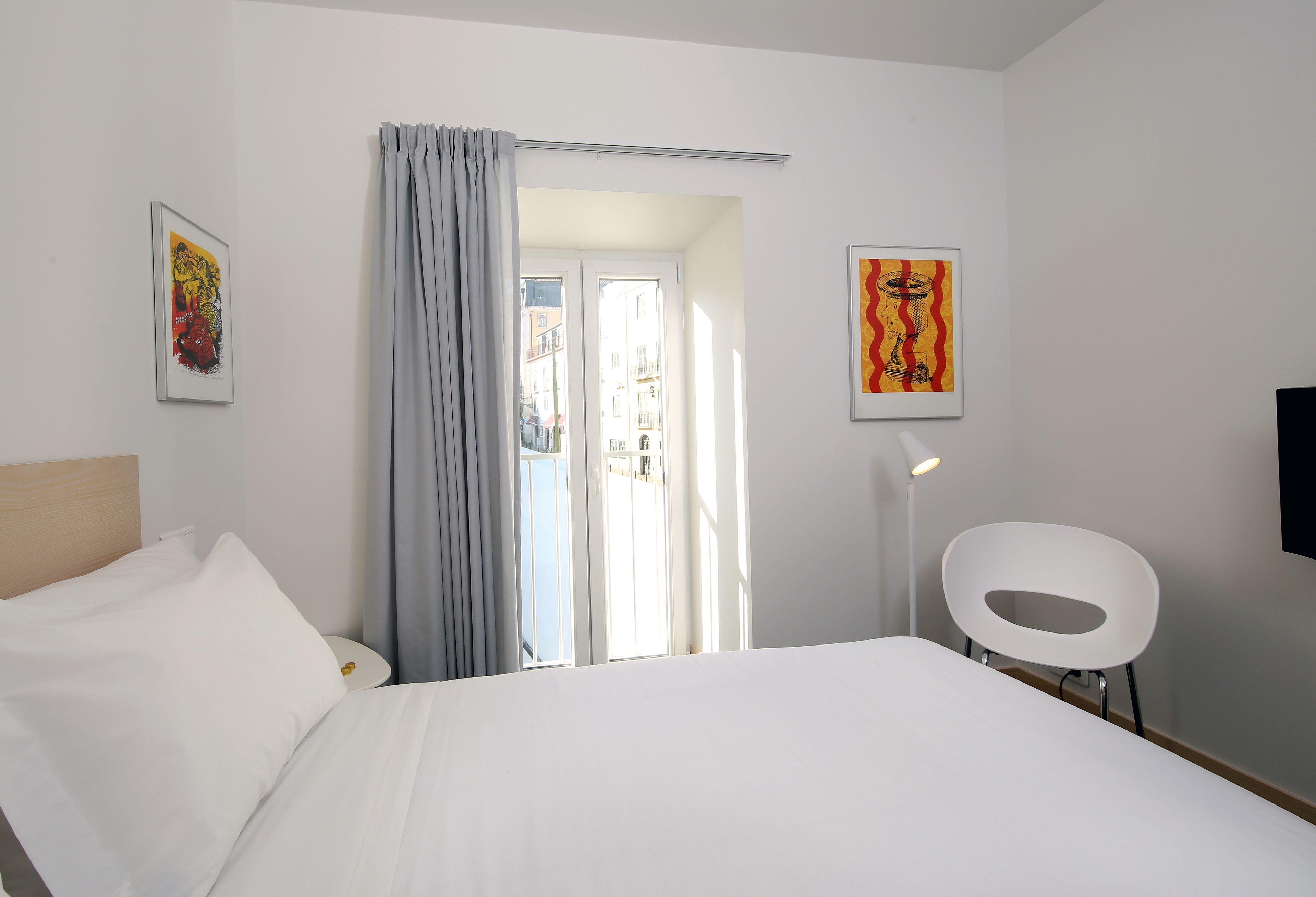 A hotel room with a bed, a chair, and two framed artworks on the walls.