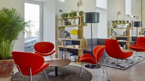 Een modern interieur met rode stoelen, een ronde tafel en een boekenkast vol boeken en planten.