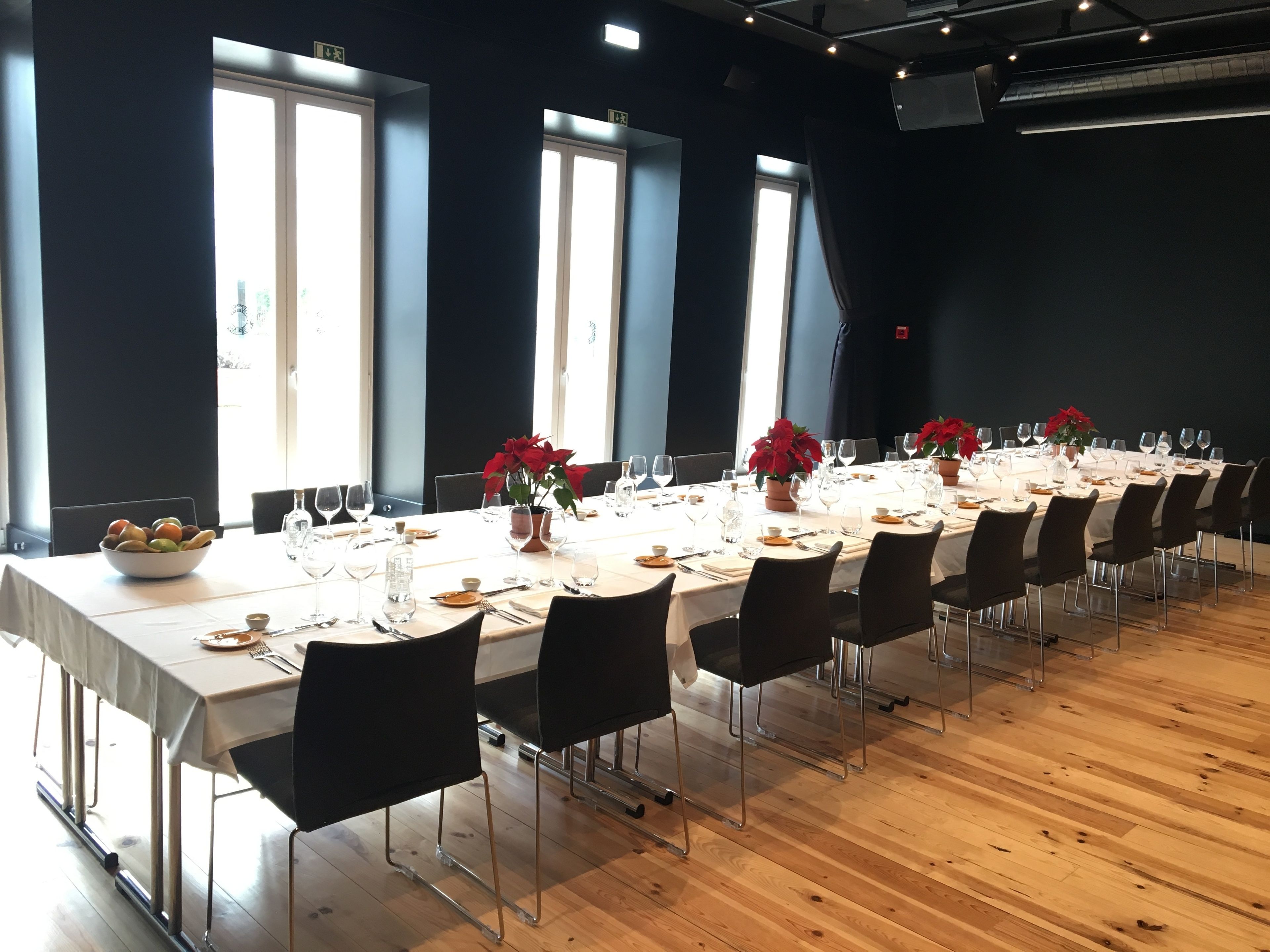 A long dining table set with chairs, large windows, and potted plants.