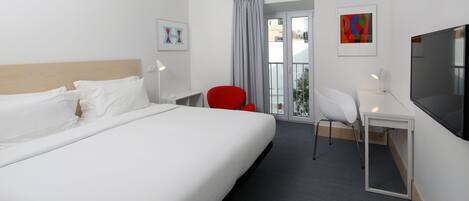 A hotel room with a bed, a desk, a TV, a chair, and a balcony with a view.
