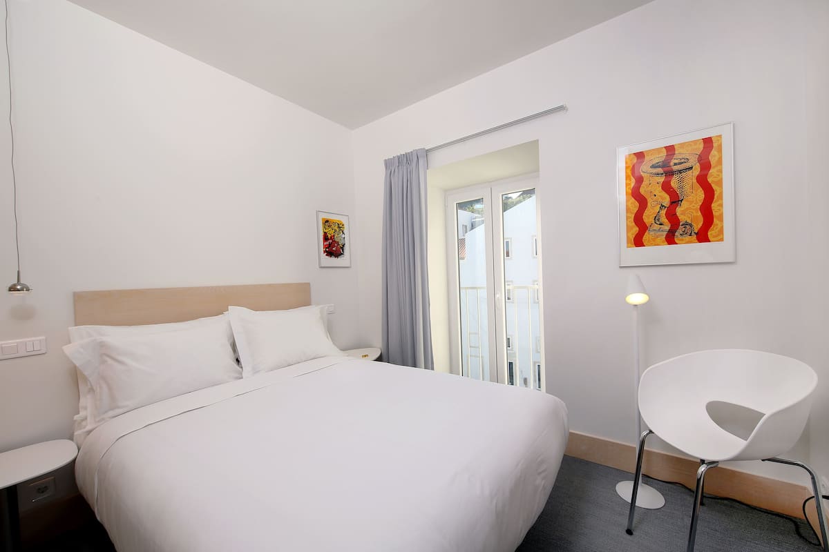 Una habitación de hotel con una cama, una mesita de noche, una silla y obras de arte en las paredes.