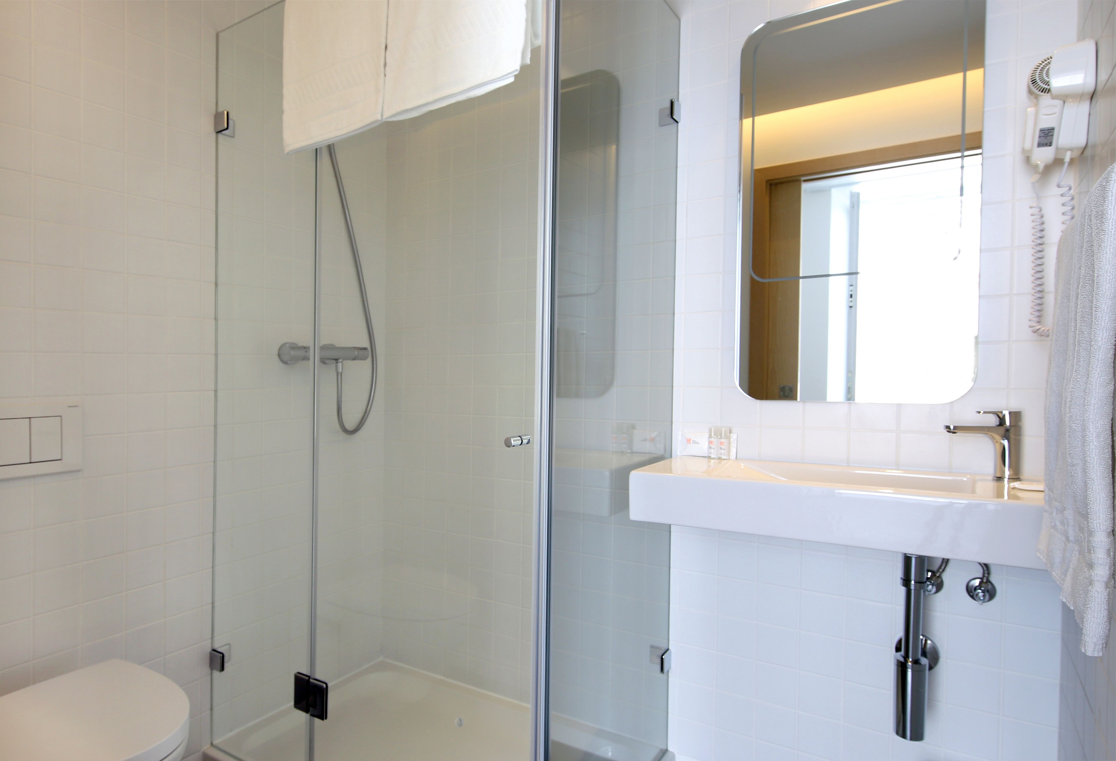 A modern bathroom with a glass-enclosed shower, a white sink with a mirror, and a toilet.