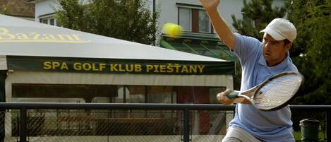Un tenista en acción en una cancha de arcilla, con un edificio que dice "SPA GOLF KLUB PIESTANY" al fondo.