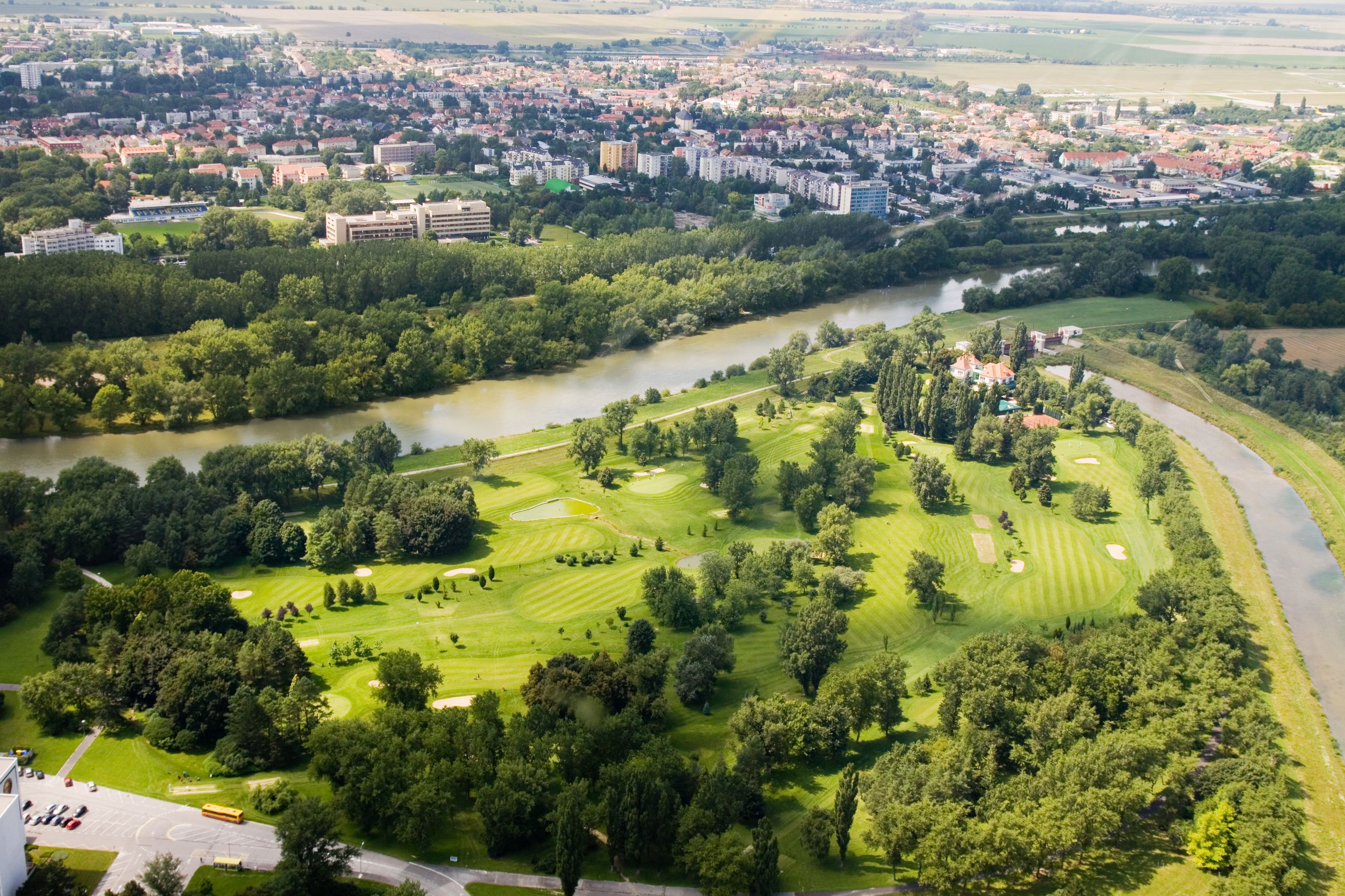 En vy över en golfbana från ovan, med en flod som rinner genom den, omgiven av bostadshus och grönområden.