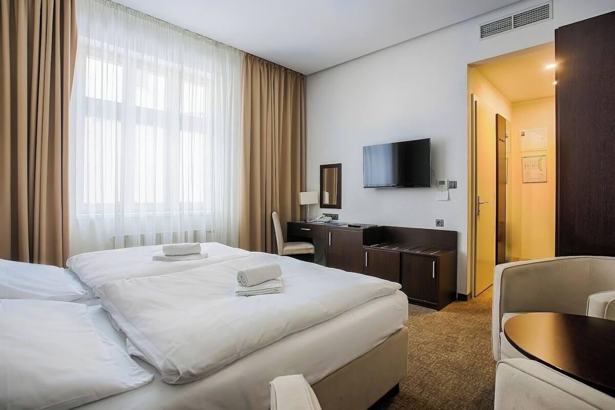Une chambre d’hôtel avec deux lits, un bureau, une chaise, une télévision et une porte donnant sur une autre pièce.