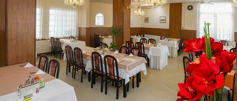 Un comedor con varias mesas y sillas, ventiladores de techo, candelabros y una planta en maceta.