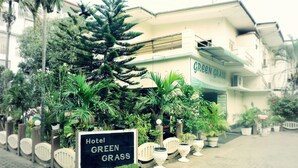 Un hotel llamado 'Hotel Green Grass' con un letrero, rodeado de abundante follaje y plantas en macetas.