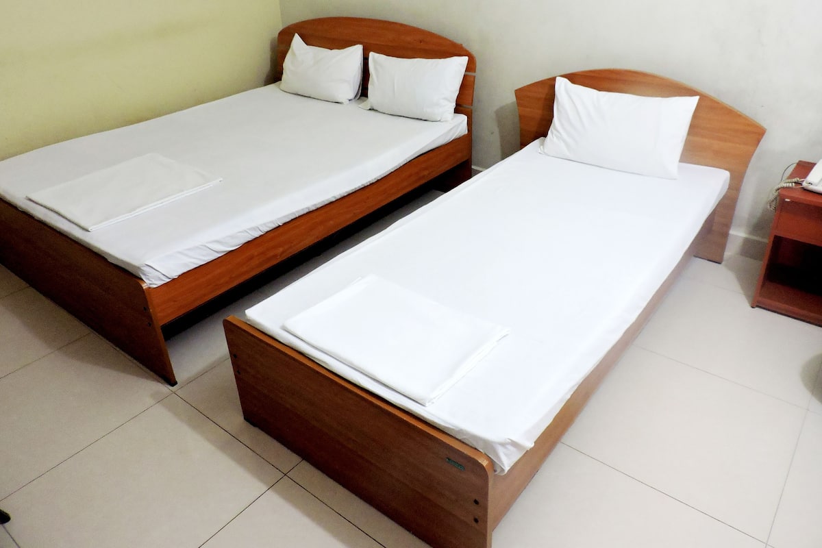 Two wooden beds with white linens and pillows, a bedside table with a phone, and a light-colored wall.